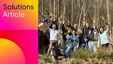 Team der FI-SP pflanzt im Wald Setzlinge, hält Spaten hoch – Baumpflanzaktion.