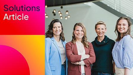 Vier Frauen nebeneinander, alle freundlich lächelnd in lockerer Business-Kleidung.