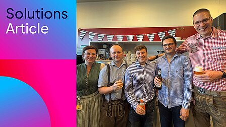 Fünf Personen stehen in Dirndl, Lederhosen und karierten Hemden mit Getränken vor einer blau-weißen Wimpelkette; links steht „Solutions Article“.