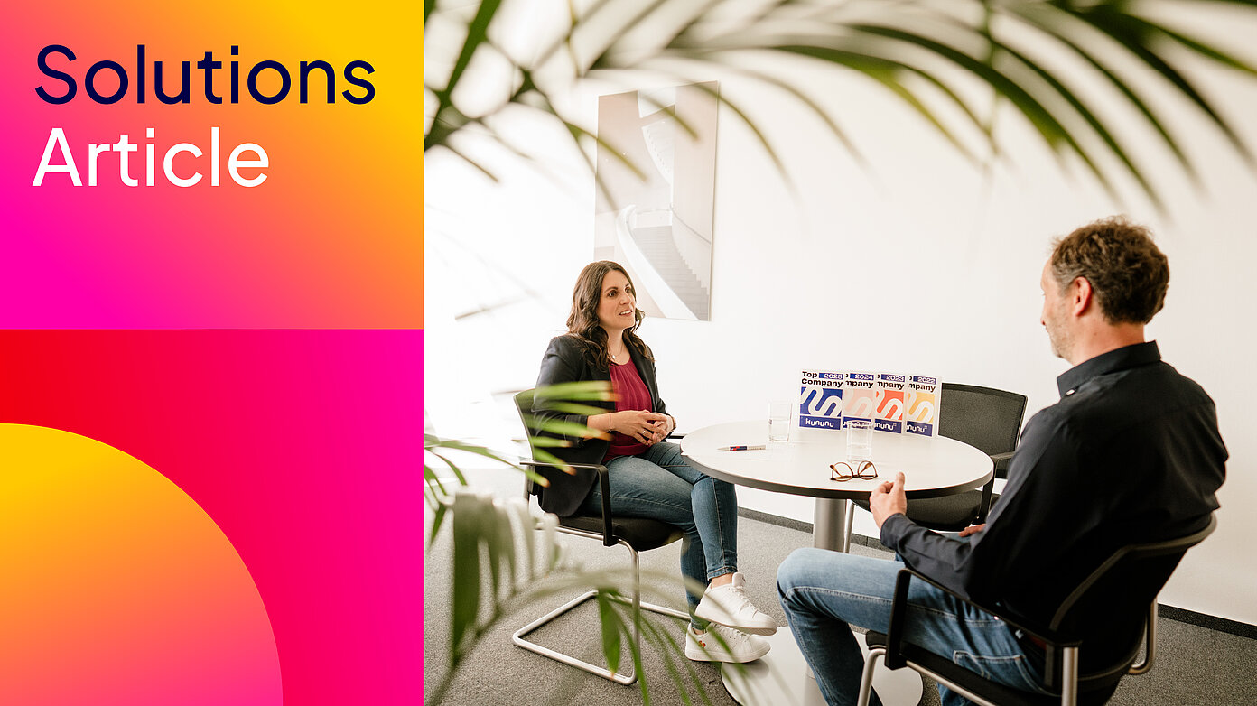 Zwei Personen im Besprechungsraum; Kununu-Auszeichnungen am Tisch – Gehaltstransparenz.