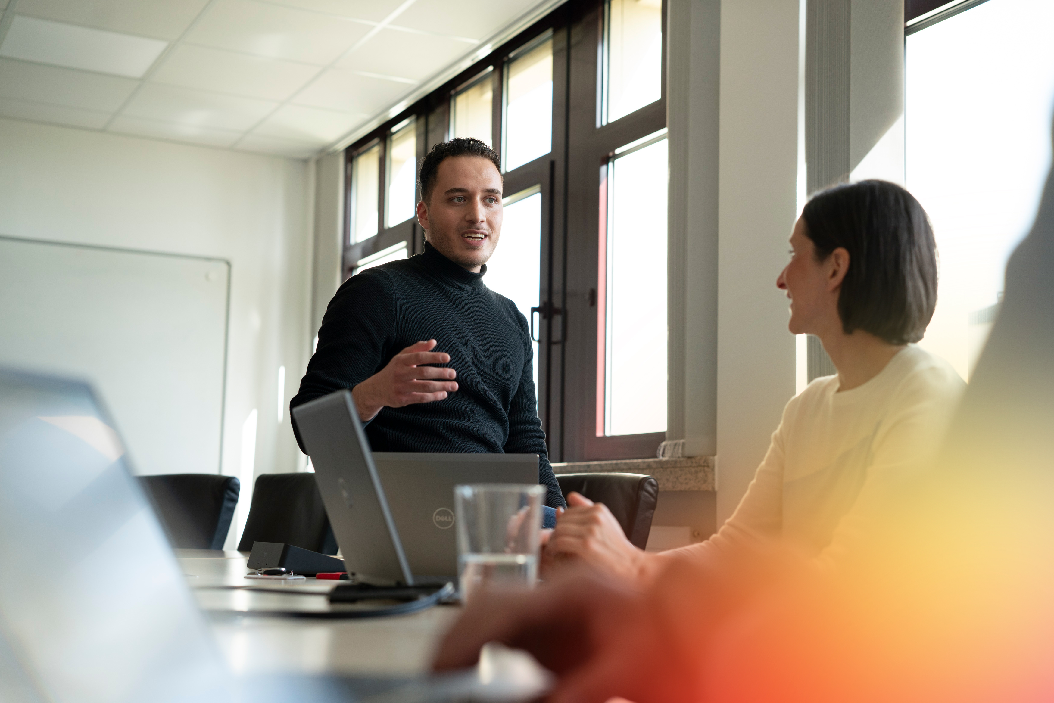 Passende Lösungen entwickeln: Beratung und Umsetzung im Team der FI-SP Mitarbeiter erklärt im Meeting passende IT-Lösungen der FI-SP, Team arbeitet am Laptop.