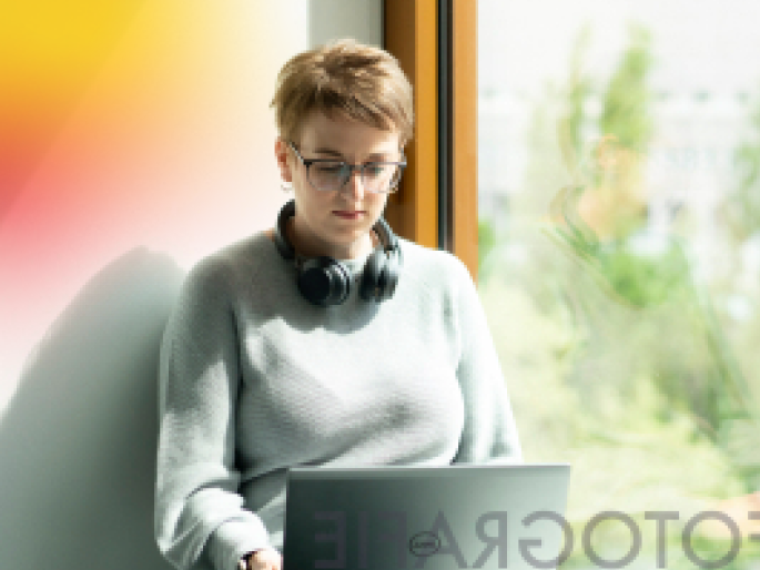 Eine junge Frau mit kurzen Haaren sitzt mit Laptop am Fenster.